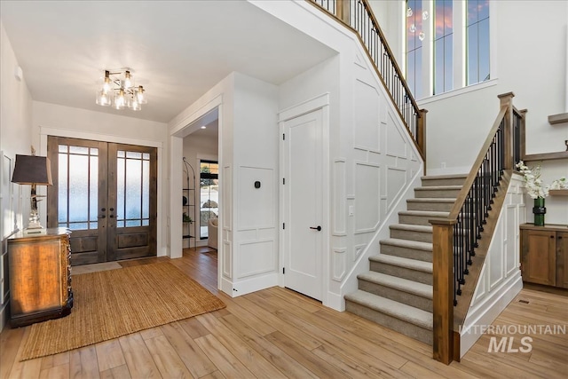 foyer entrance featuring french doors, an inviting chandelier, a high ceiling, and light wood-type flooring