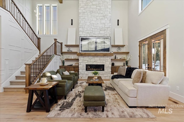 living room with french doors, a towering ceiling, a fireplace, and light wood-type flooring