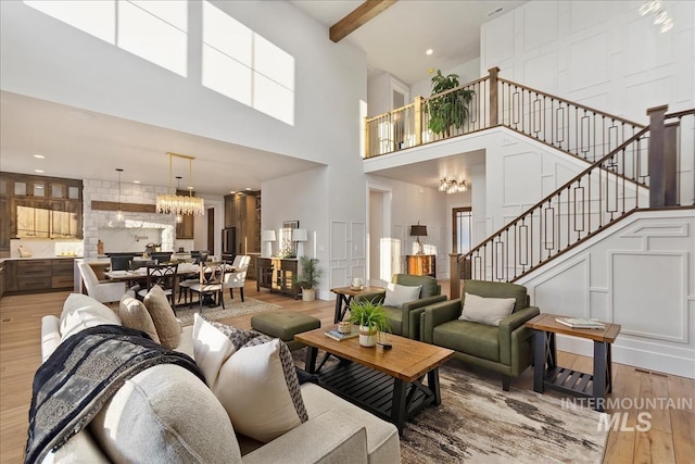 living room featuring beam ceiling, a towering ceiling, hardwood / wood-style floors, and an inviting chandelier