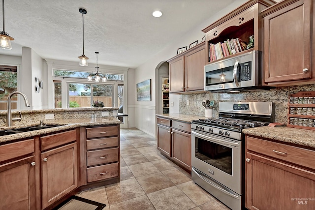 kitchen with sink, appliances with stainless steel finishes, hanging light fixtures, backsplash, and light stone counters