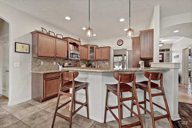 kitchen with a kitchen bar, tasteful backsplash, kitchen peninsula, pendant lighting, and light stone countertops