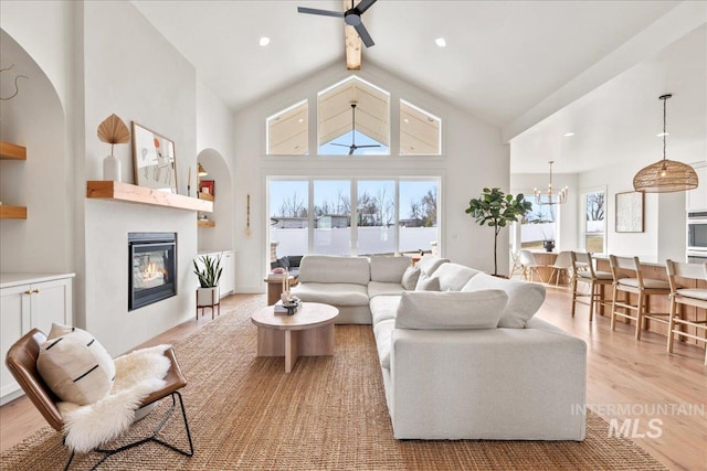 living area with high vaulted ceiling, recessed lighting, ceiling fan with notable chandelier, wood finished floors, and a glass covered fireplace