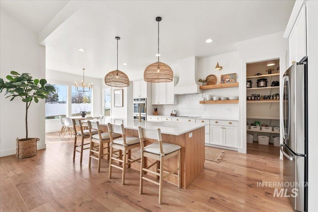 kitchen with light wood finished floors, custom range hood, appliances with stainless steel finishes, and light countertops