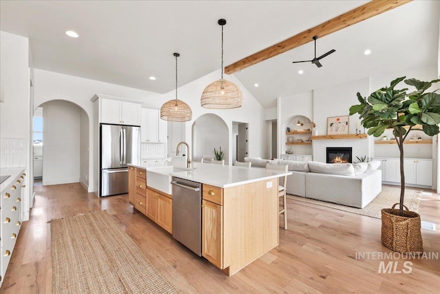 kitchen with arched walkways, stainless steel appliances, a sink, light wood-style floors, and beam ceiling