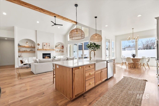 kitchen with light wood finished floors, a glass covered fireplace, beamed ceiling, a sink, and stainless steel dishwasher