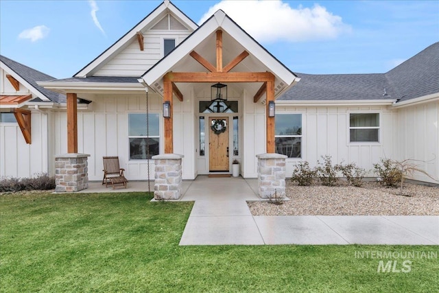 view of exterior entry featuring roof with shingles, board and batten siding, and a yard