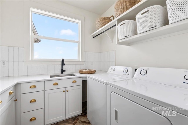 laundry room featuring brick floor, cabinet space, a sink, and washer and clothes dryer