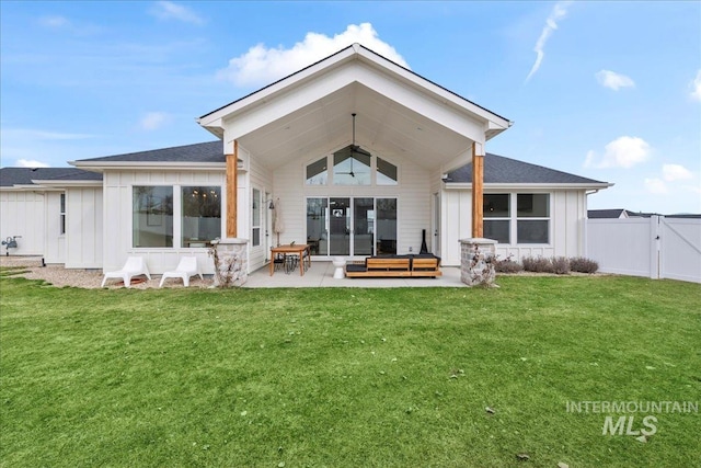 rear view of property with board and batten siding, a patio area, a lawn, and fence