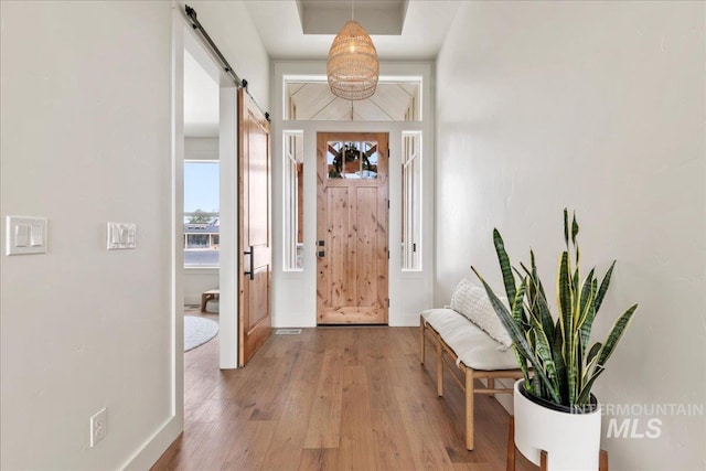 foyer with light wood finished floors, a barn door, and baseboards