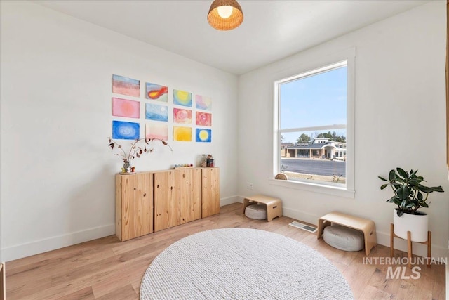 living area with light wood-type flooring, visible vents, and baseboards