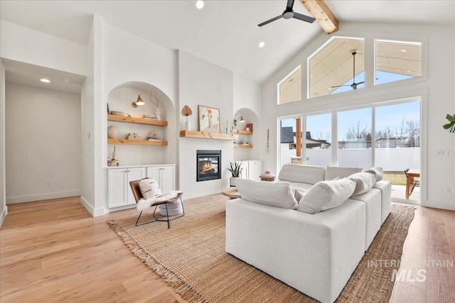 living area with high vaulted ceiling, a glass covered fireplace, a ceiling fan, and light wood-style floors