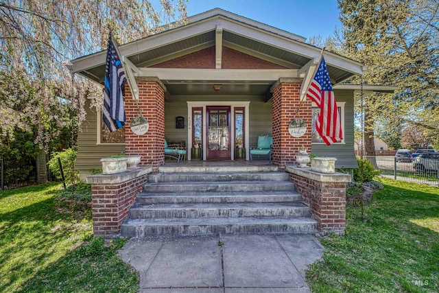 view of front of home featuring brick siding, a porch, fence, and a front lawn