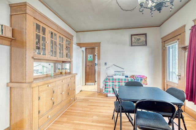 dining area with light wood-type flooring, an inviting chandelier, and crown molding