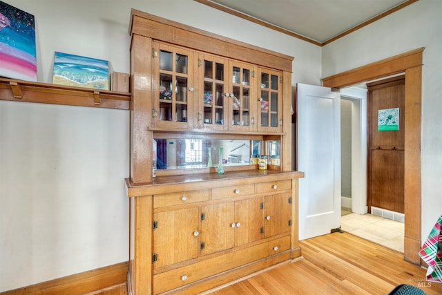 interior space with visible vents, light wood-style flooring, ornamental molding, brown cabinetry, and glass insert cabinets