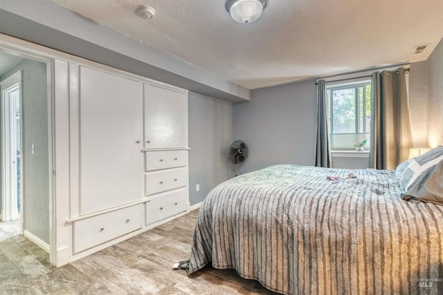 bedroom with visible vents, baseboards, a textured ceiling, and light wood-style flooring