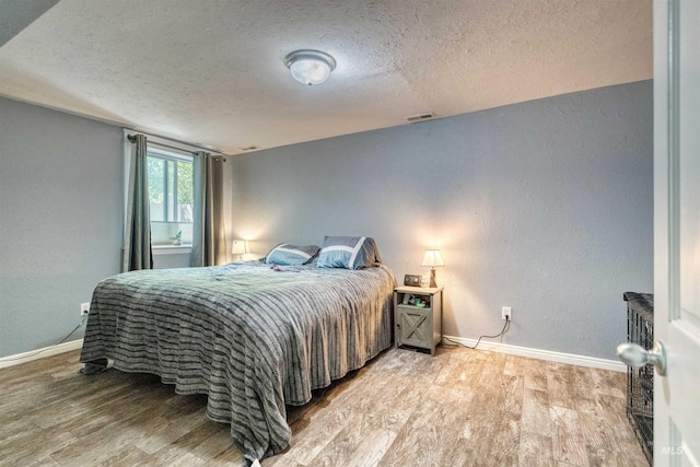 bedroom with baseboards, wood finished floors, visible vents, and a textured ceiling