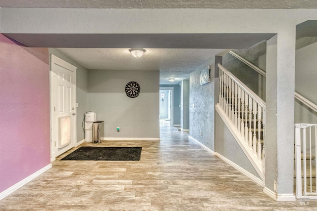 corridor with baseboards, a textured ceiling, wood finished floors, and stairs