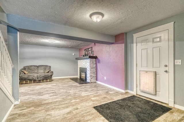 interior space featuring a brick fireplace, a textured ceiling, baseboards, and wood finished floors