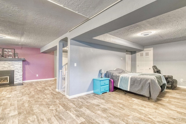 bedroom featuring a fireplace with flush hearth, a textured ceiling, baseboards, and wood finished floors