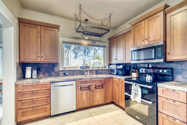 kitchen featuring tile countertops, brown cabinetry, a sink, stainless steel appliances, and tasteful backsplash