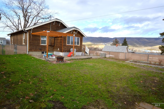 rear view of house featuring a mountain view, a fire pit, and a lawn