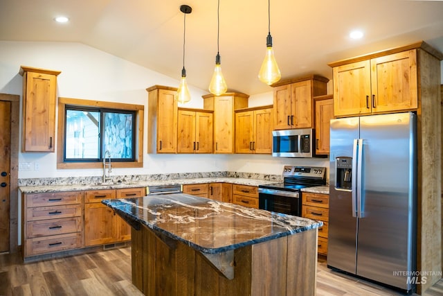 kitchen featuring pendant lighting, lofted ceiling, a kitchen island, appliances with stainless steel finishes, and dark stone countertops