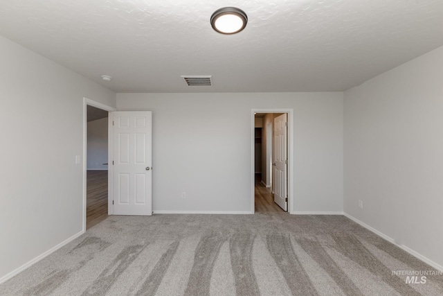 carpeted spare room with visible vents, baseboards, and a textured ceiling