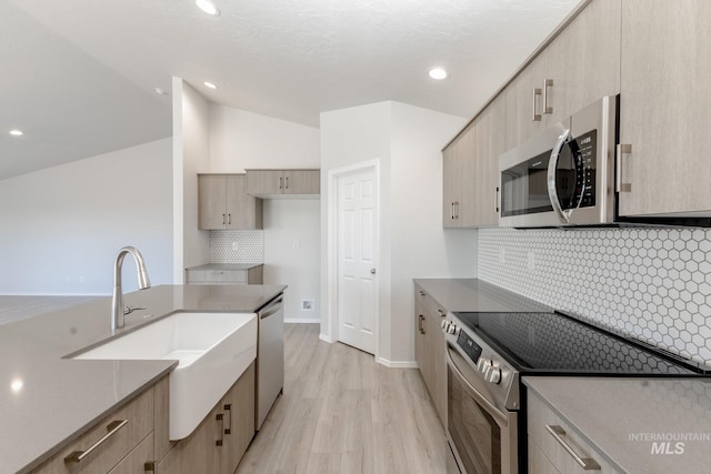 kitchen with light wood-style flooring, light brown cabinetry, a sink, appliances with stainless steel finishes, and vaulted ceiling