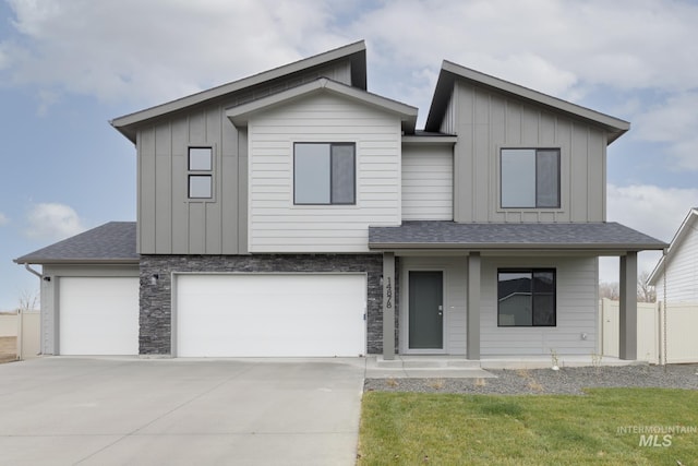 modern home with stone siding, fence, board and batten siding, concrete driveway, and a shingled roof