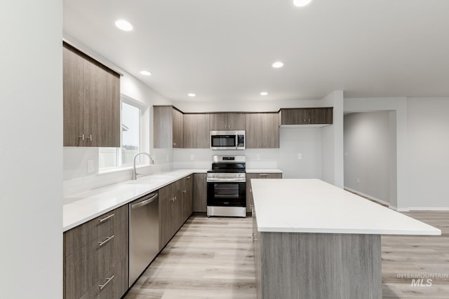 kitchen with a sink, a kitchen island, light wood-style floors, stainless steel appliances, and modern cabinets