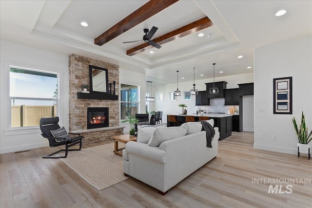 living room with light wood-type flooring, beam ceiling, a fireplace, and a raised ceiling