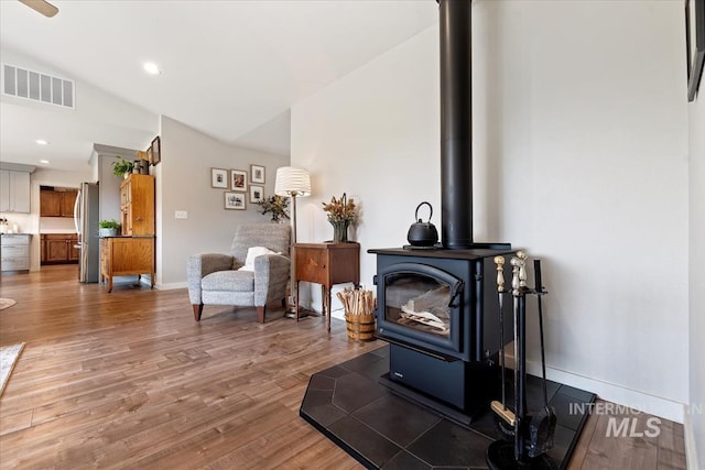 living area featuring recessed lighting, visible vents, a wood stove, light wood-type flooring, and baseboards