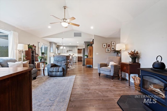 living area featuring visible vents, ceiling fan, wood finished floors, a wood stove, and vaulted ceiling