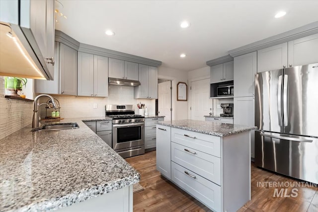 kitchen with light stone counters, stainless steel appliances, gray cabinets, a sink, and under cabinet range hood