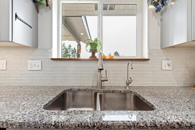 kitchen with light stone countertops, tasteful backsplash, white cabinets, and a sink