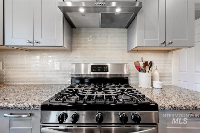 kitchen with wall chimney range hood, gas stove, light stone counters, and decorative backsplash