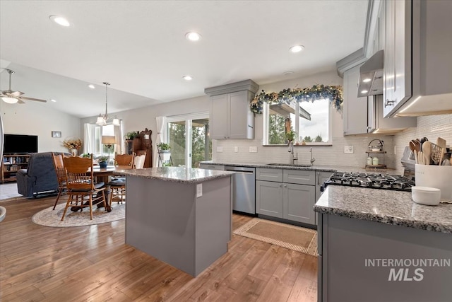 kitchen with dishwasher, vaulted ceiling, gray cabinetry, wall chimney range hood, and a sink