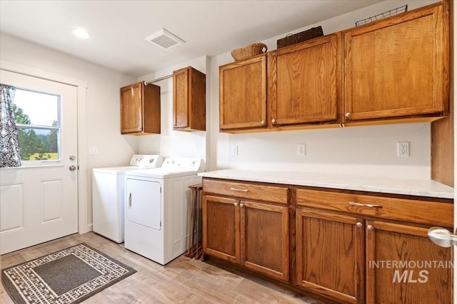 clothes washing area with visible vents, washing machine and dryer, cabinet space, and light wood-style floors