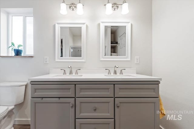 bathroom with a chandelier, double vanity, a sink, and toilet