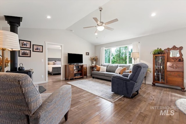 living area featuring lofted ceiling, a wood stove, ceiling fan, and wood finished floors