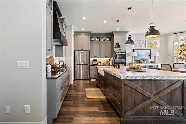 kitchen featuring stainless steel appliances, backsplash, a spacious island, dark wood-type flooring, and hanging light fixtures