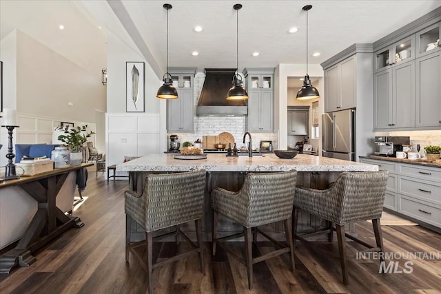 kitchen with premium range hood, gray cabinets, high end refrigerator, and a kitchen island with sink