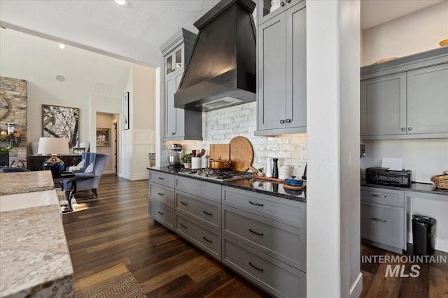 kitchen featuring tasteful backsplash, gray cabinets, dark wood-type flooring, custom range hood, and dark stone counters