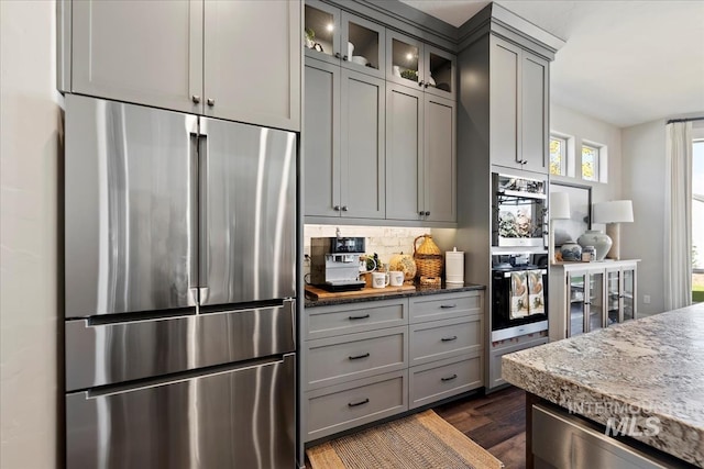 kitchen featuring decorative backsplash, dark stone counters, stainless steel refrigerator, and gray cabinets