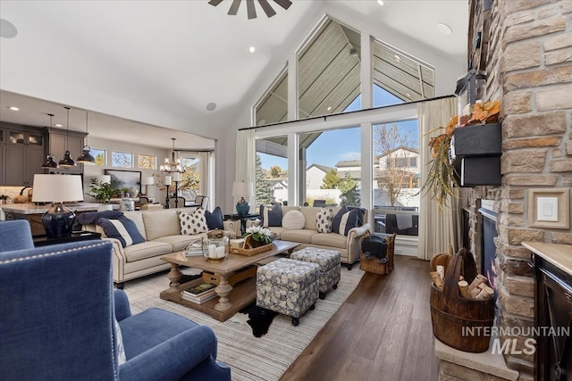 living room with high vaulted ceiling, ceiling fan with notable chandelier, a stone fireplace, and light hardwood / wood-style floors