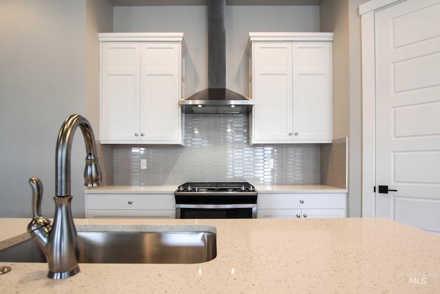 kitchen with wall chimney exhaust hood, white cabinetry, a sink, and stainless steel stove