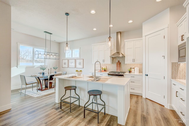 kitchen featuring appliances with stainless steel finishes, light countertops, an island with sink, and wall chimney exhaust hood