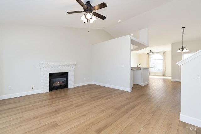 unfurnished living room with a fireplace, sink, light wood-type flooring, high vaulted ceiling, and ceiling fan with notable chandelier