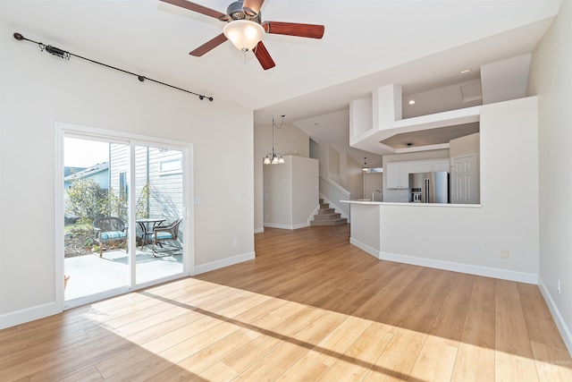 unfurnished living room with ceiling fan with notable chandelier and light hardwood / wood-style flooring