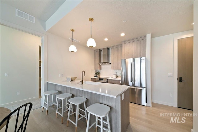 kitchen featuring sink, wall chimney exhaust hood, stainless steel appliances, kitchen peninsula, and decorative light fixtures